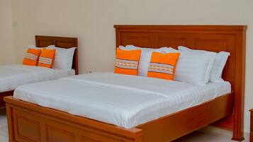 Two single beds with wooden headboards and white bedding, one with orange pillows and the other with white pillows.