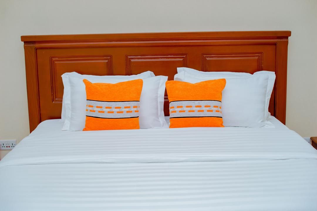 A bed with white bedding and two pillows with orange and white patterns.
