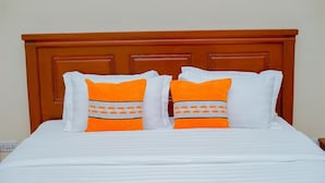 A bed with white bedding and two pillows with orange and white patterns. - The Mana Hotel (Zanzibar)
