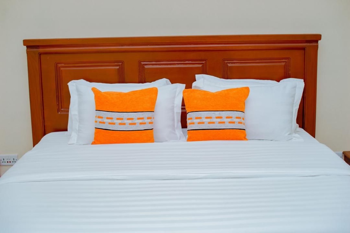 Un lit avec une literie blanche et deux oreillers aux motifs orange et blanc.