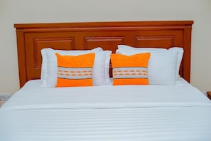 Un lit avec une literie blanche et deux oreillers aux motifs orange et blanc.