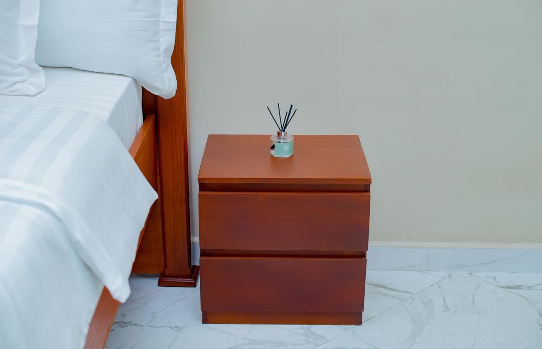 Una cama bien tendida con sábanas blancas y una mesita de noche de madera con cajones.