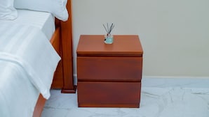 A neatly made bed with white linens and a wooden nightstand with drawers. - The Mana Hotel (Zanzibar)