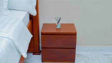 Un letto rifatto con lenzuola bianche e un comodino in legno con cassetti.