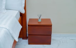 Un lit bien fait, avec du linge de lit blanc et une table de chevet en bois dotée de tiroirs.