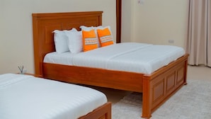 A double bed with a wooden headboard and two pillows, one white and one orange, in a room with a beige carpet. - The Mana Hotel (Zanzibar)