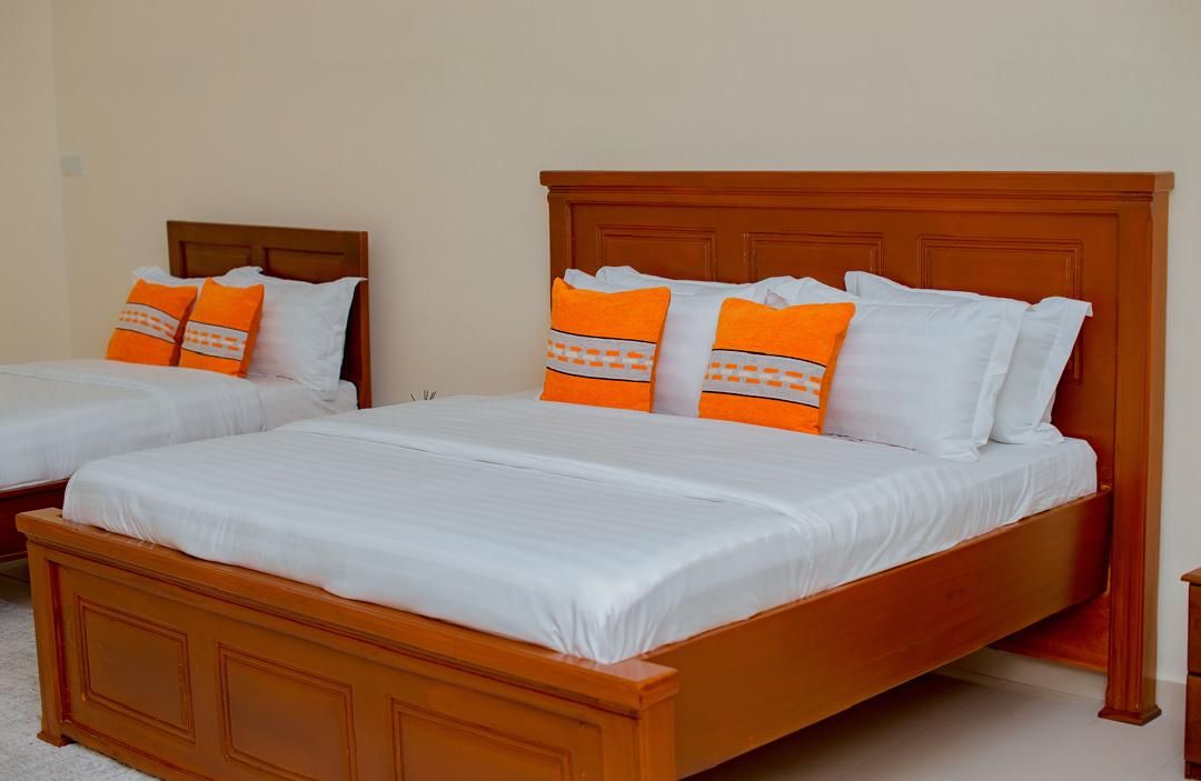 Two single beds with wooden headboards and white bedding, one with orange pillows and the other with white pillows.