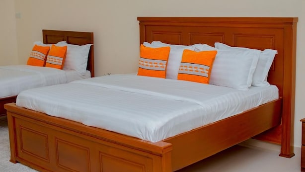 Two single beds with wooden headboards and white bedding, one with orange pillows and the other with white pillows. - The Mana Hotel (Zanzibar)