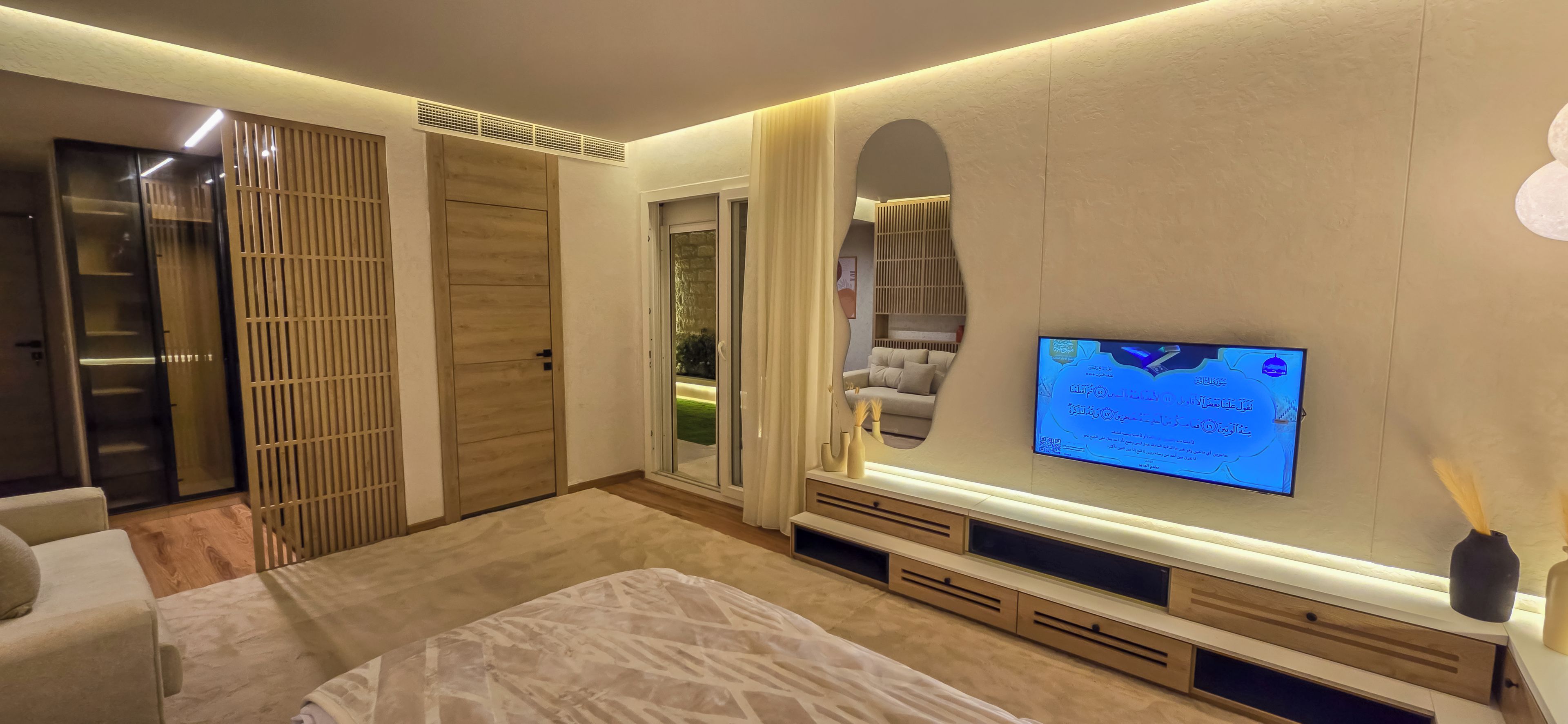 A bedroom with a bed, a TV mounted on the wall, a sliding door closet, and a large mirror.