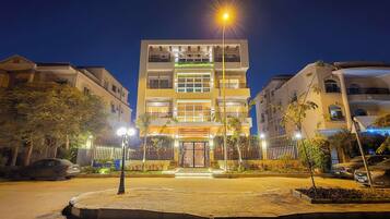 A multi-story hotel with a gated entrance, illuminated by street lamps, surrounded by parked cars and trees.