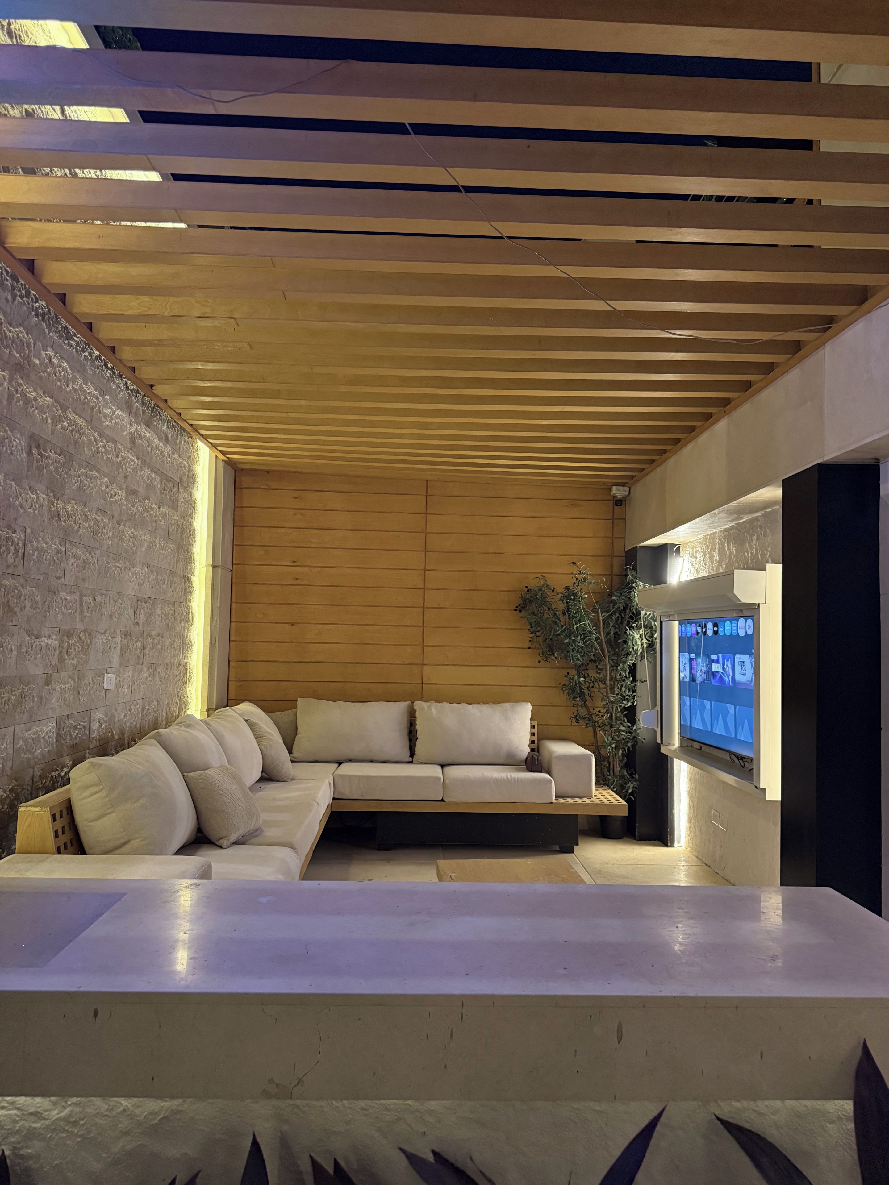 A modern interior with a sectional sofa, a flat-screen TV, and a wooden ceiling.