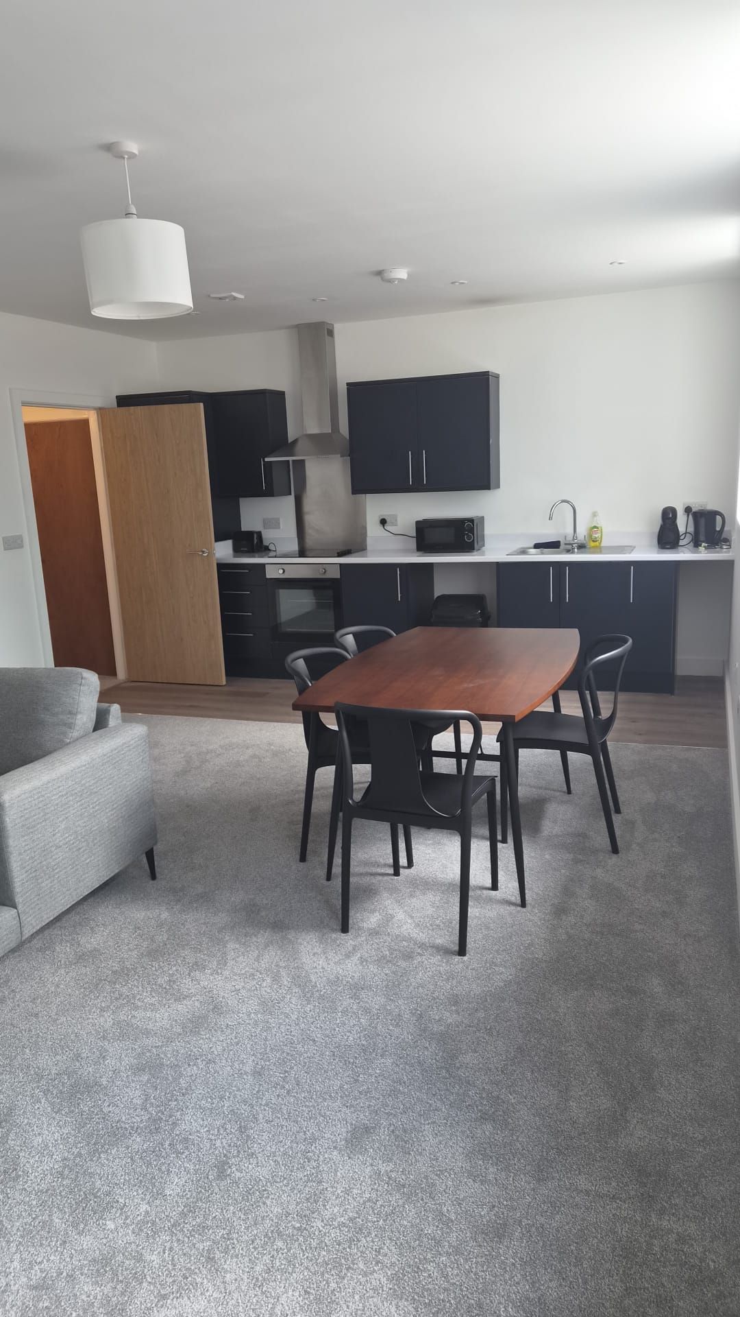 Een moderne keuken met donkere kasten, een centraal eiland en een eethoek met een houten tafel en stoelen.