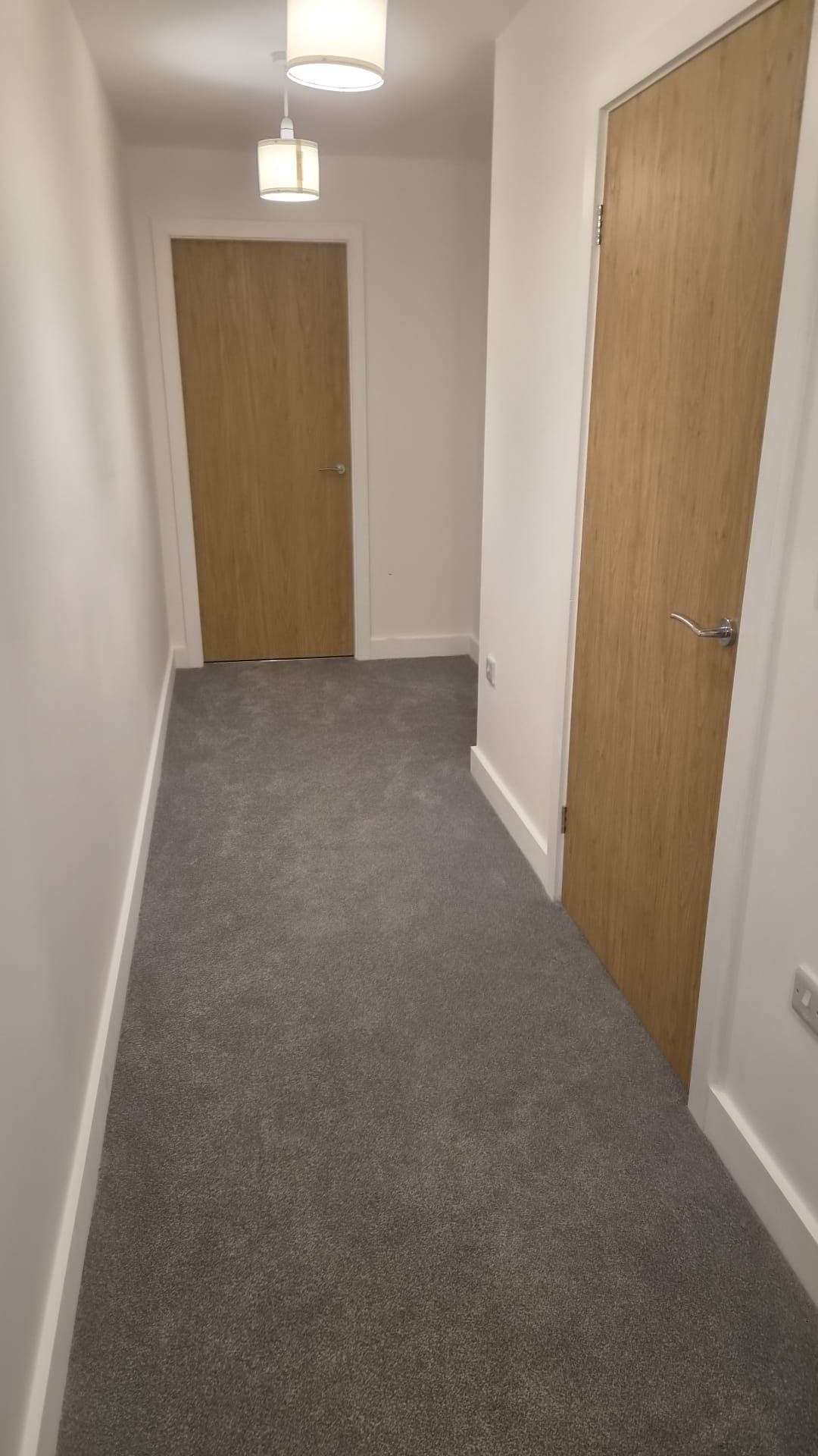 A narrow hallway with carpeted flooring and wooden doors on either side.