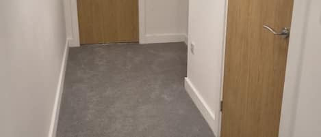 A narrow hallway with carpeted flooring and wooden doors on either side.