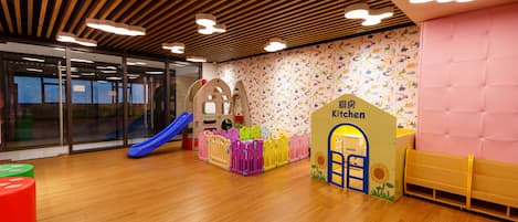 Un espace de jeux pour enfants avec un toboggan, des barrières de sécurité et un panneau indiquant la présence d’une petite cuisine.