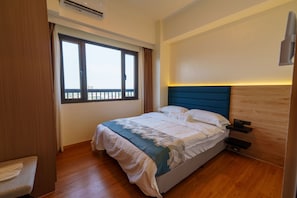 Een hotelkamer met een bed, een raam, een nachtkastje en een wandairconditioner.