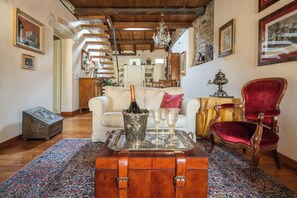 Un vaste salon doté d’un plafond en bois, d’un tapis à motifs, d’une malle ancienne, d’un fauteuil en velours rouge et d’un lustre.