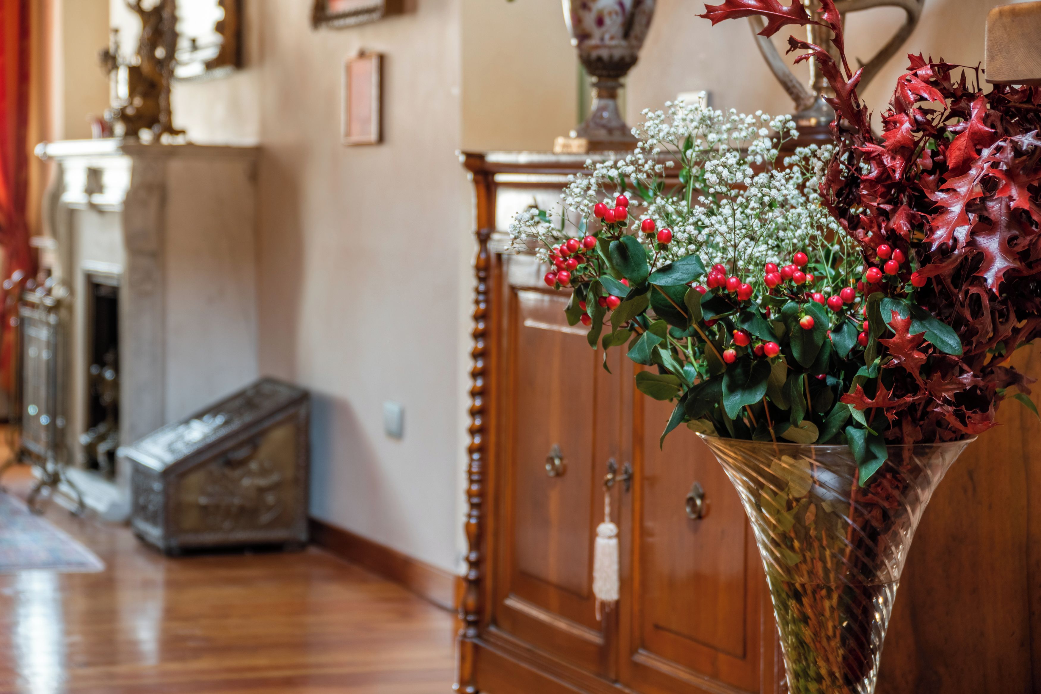 Ein Zimmer mit einem Holzkabinett, einer Vase mit roten Beeren und weißen Blumen sowie einem Kamin.