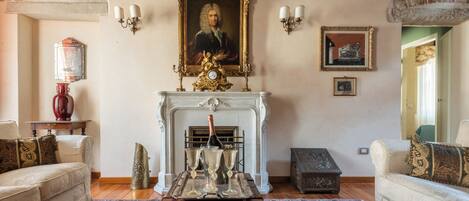 A traditional living room with a fireplace, a portrait above it, and a vintage trunk in the center.