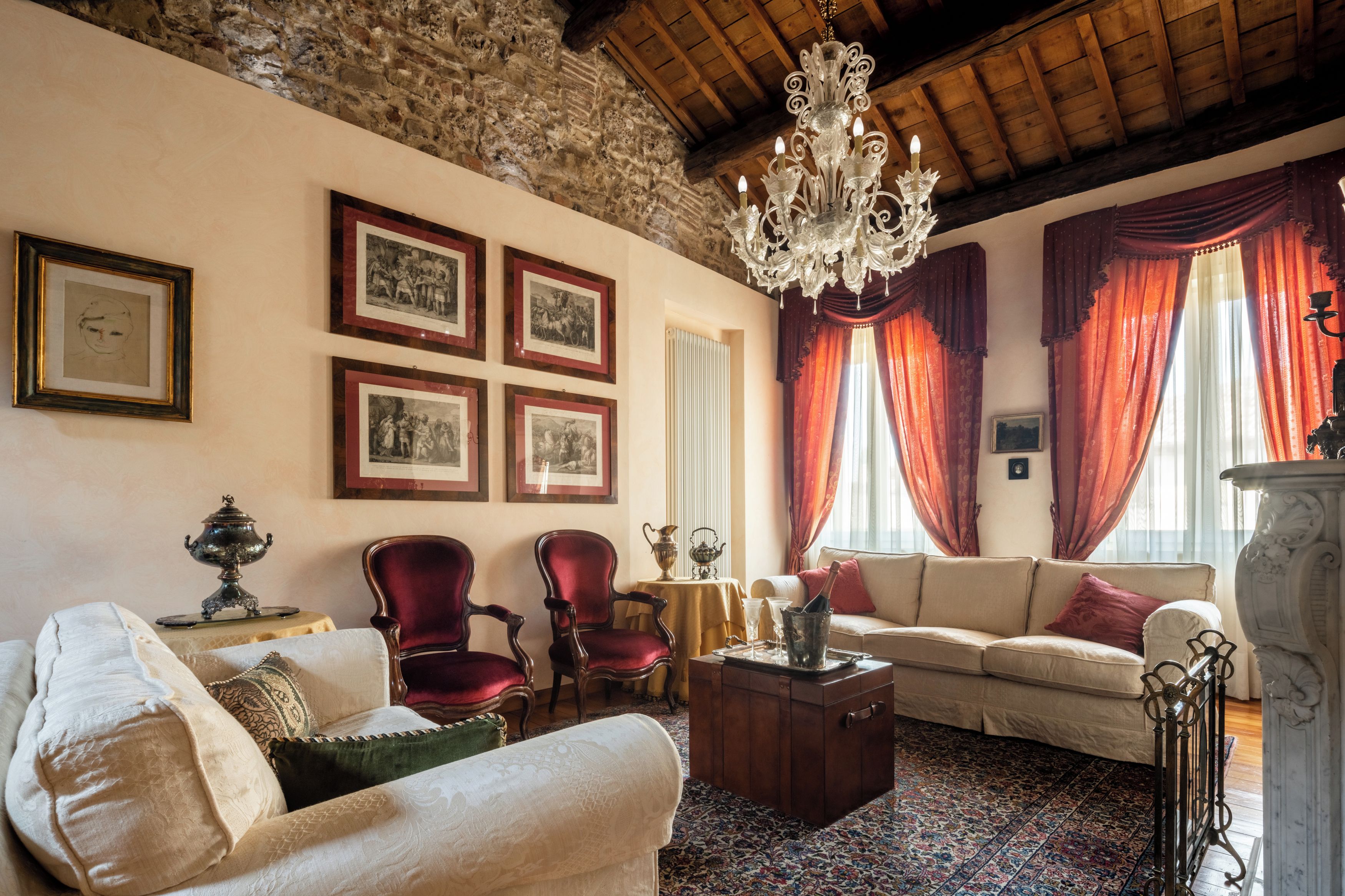 Une pièce au décor traditionnel, avec un mur en pierre, un lustre, des rideaux rouges et un canapé.