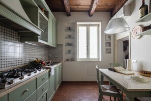 A kitchen with a gas stove, green cabinets, a window with lace curtains, and a hanging light fixture.