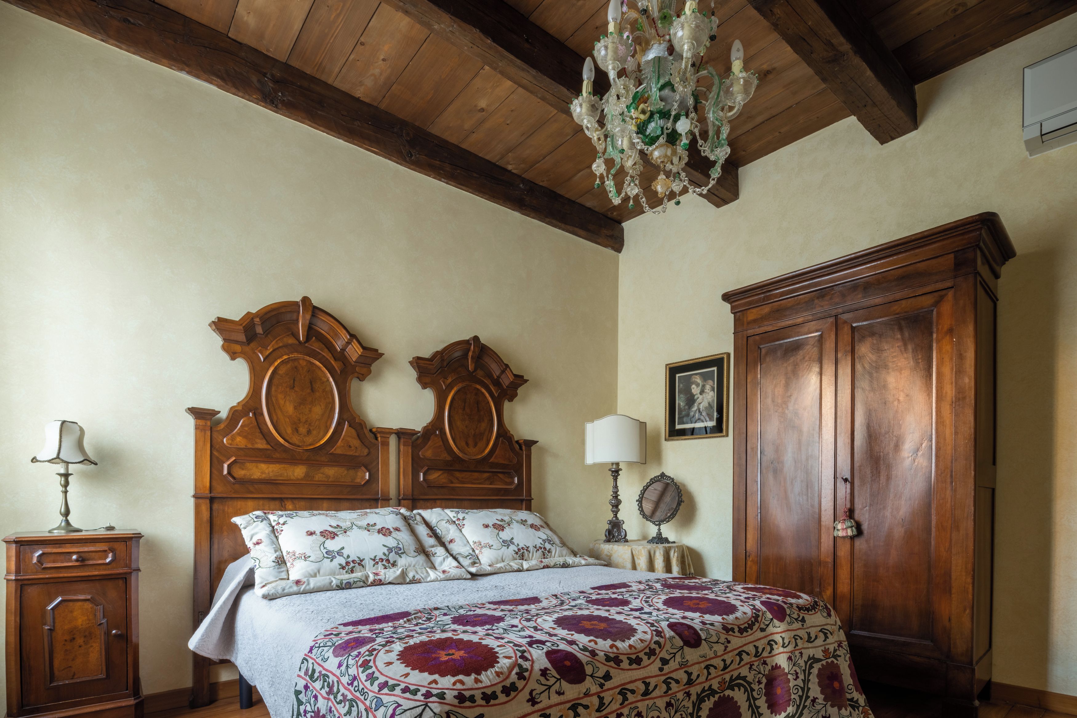 Una camera da letto con un letto di legno, un comodino, una cassettiera, un lampadario e un quadro appeso al muro.
