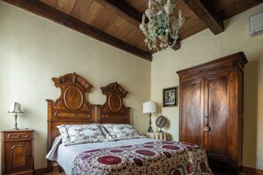 A bedroom with a wooden bed, a nightstand, a dresser, a chandelier, and a framed picture on the wall.