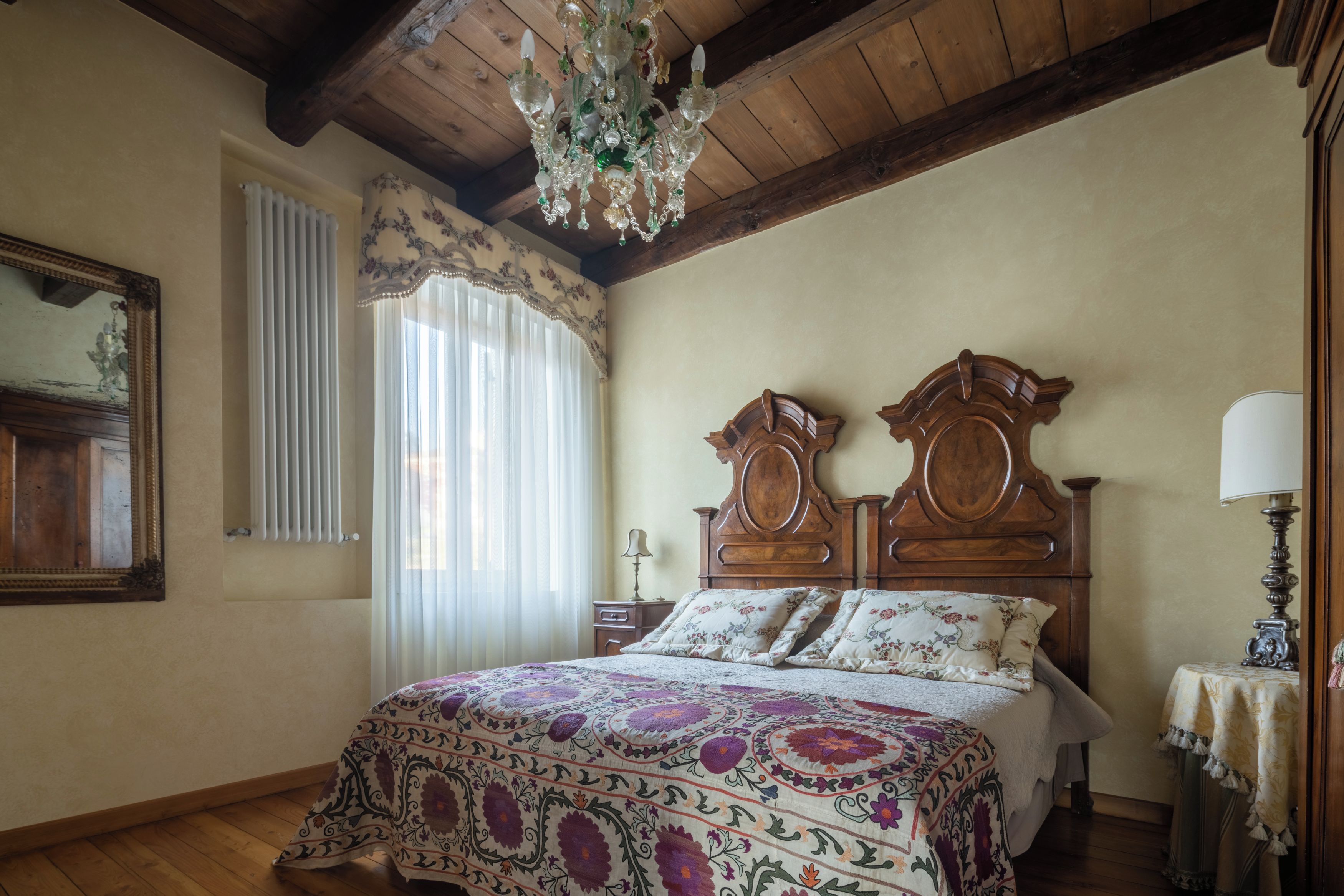 Ein Schlafzimmer mit Holzboden, einem großen Bett mit floralem Bettzeug, einer Kandelaber und einem Spiegel an der Wand.