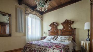 Ein Schlafzimmer mit Holzboden, einem großen Bett mit floralem Bettzeug, einer Kandelaber und einem Spiegel an der Wand.