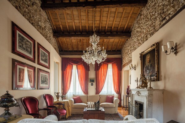 A traditional room with a wooden ceiling, a chandelier, a fireplace, and framed pictures on the walls.