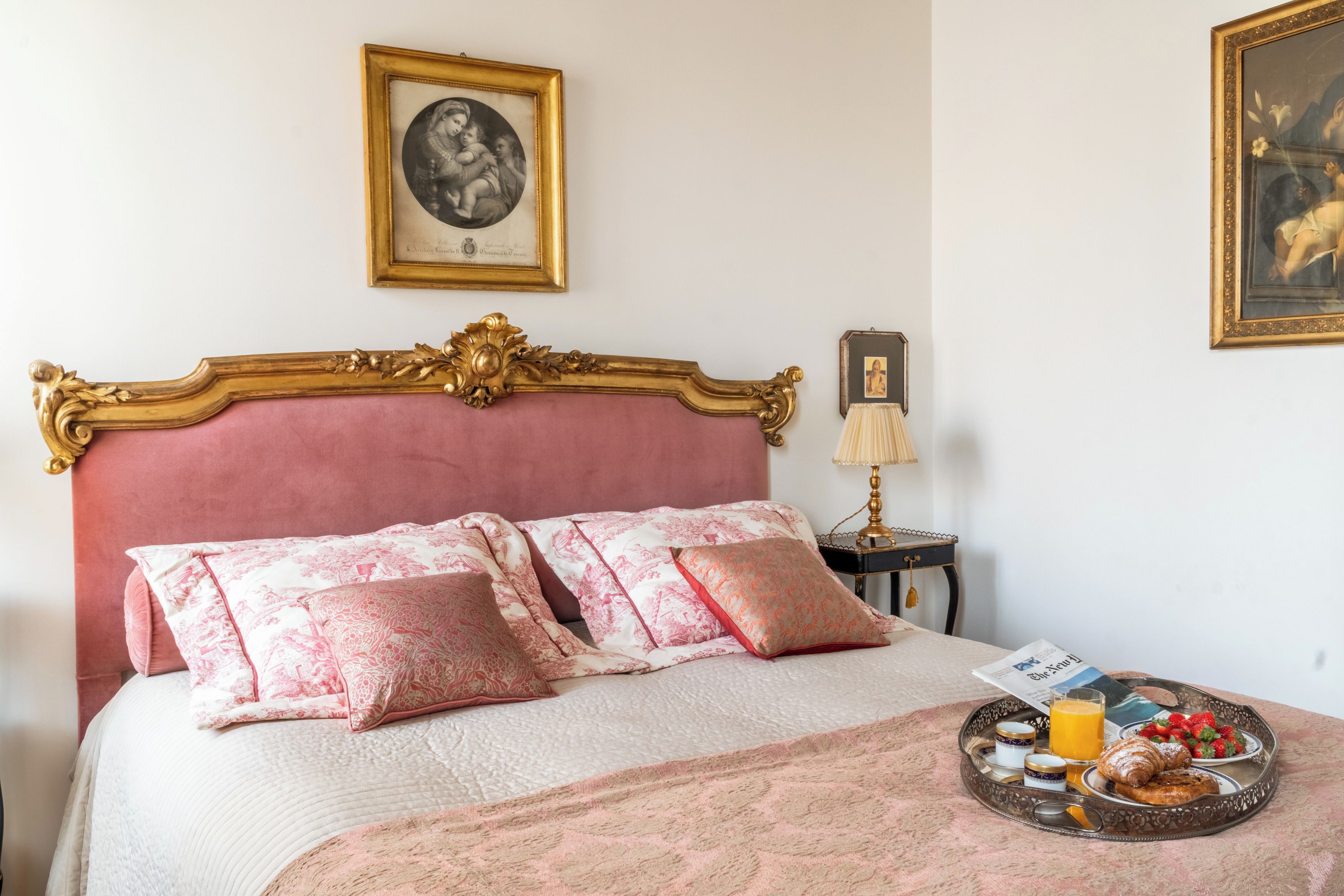 A bedroom with a large bed, a bedside table with a lamp, and a tray with breakfast items.