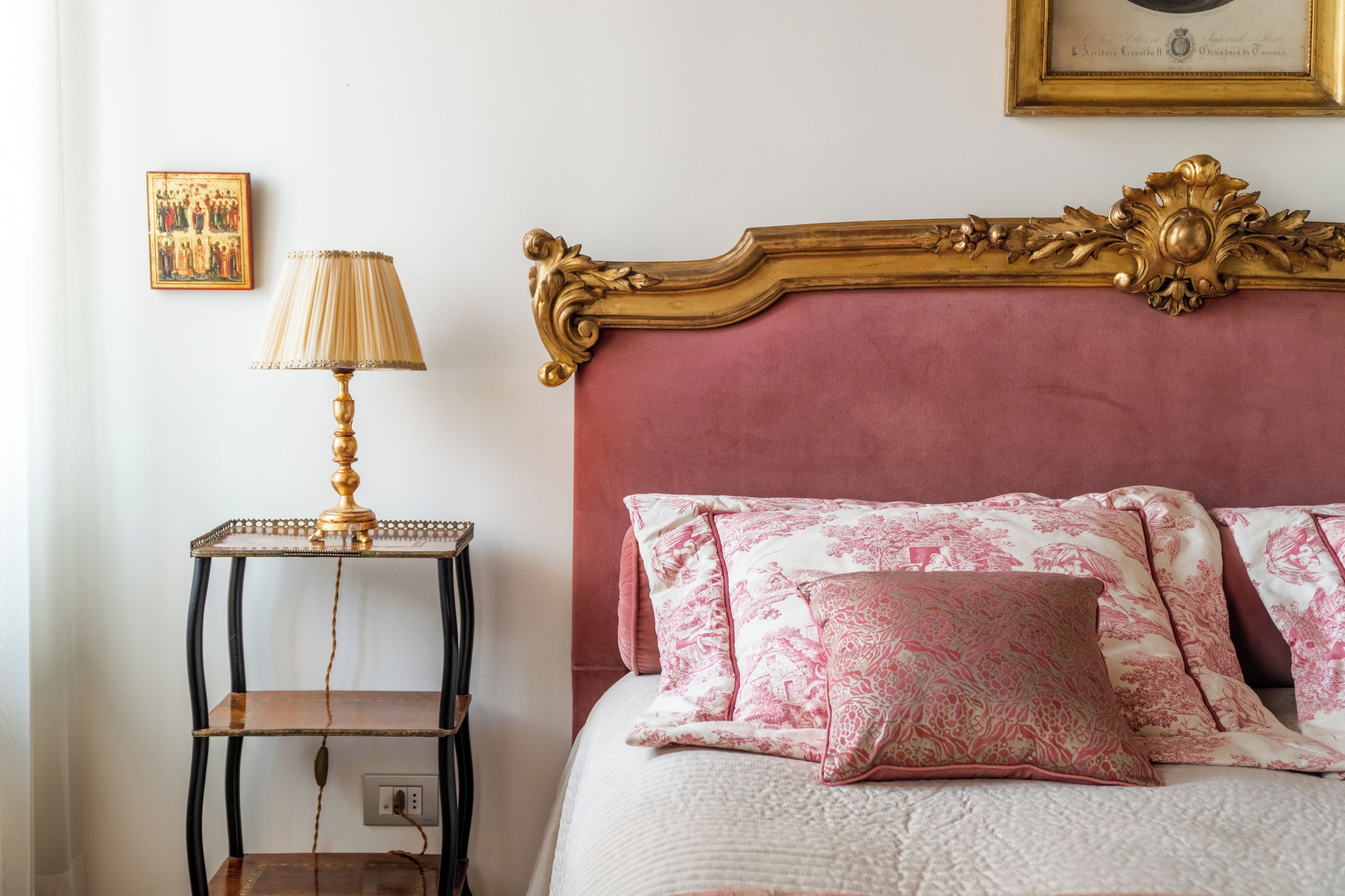 Un letto con biancheria da letto a fiori rosa e una testiera dorata decorata.