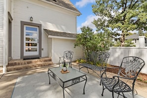 A patio with a table and chairs, a door, and a small garden area. - The Sanctuary | Old Town Retreat & Garden Oasis (Fort Collins)