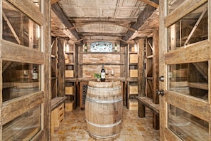 A wooden wine cellar with a barrel in the center, wooden shelves, and a wine rack above. - The Sanctuary | Old Town Retreat & Garden Oasis (Fort Collins)