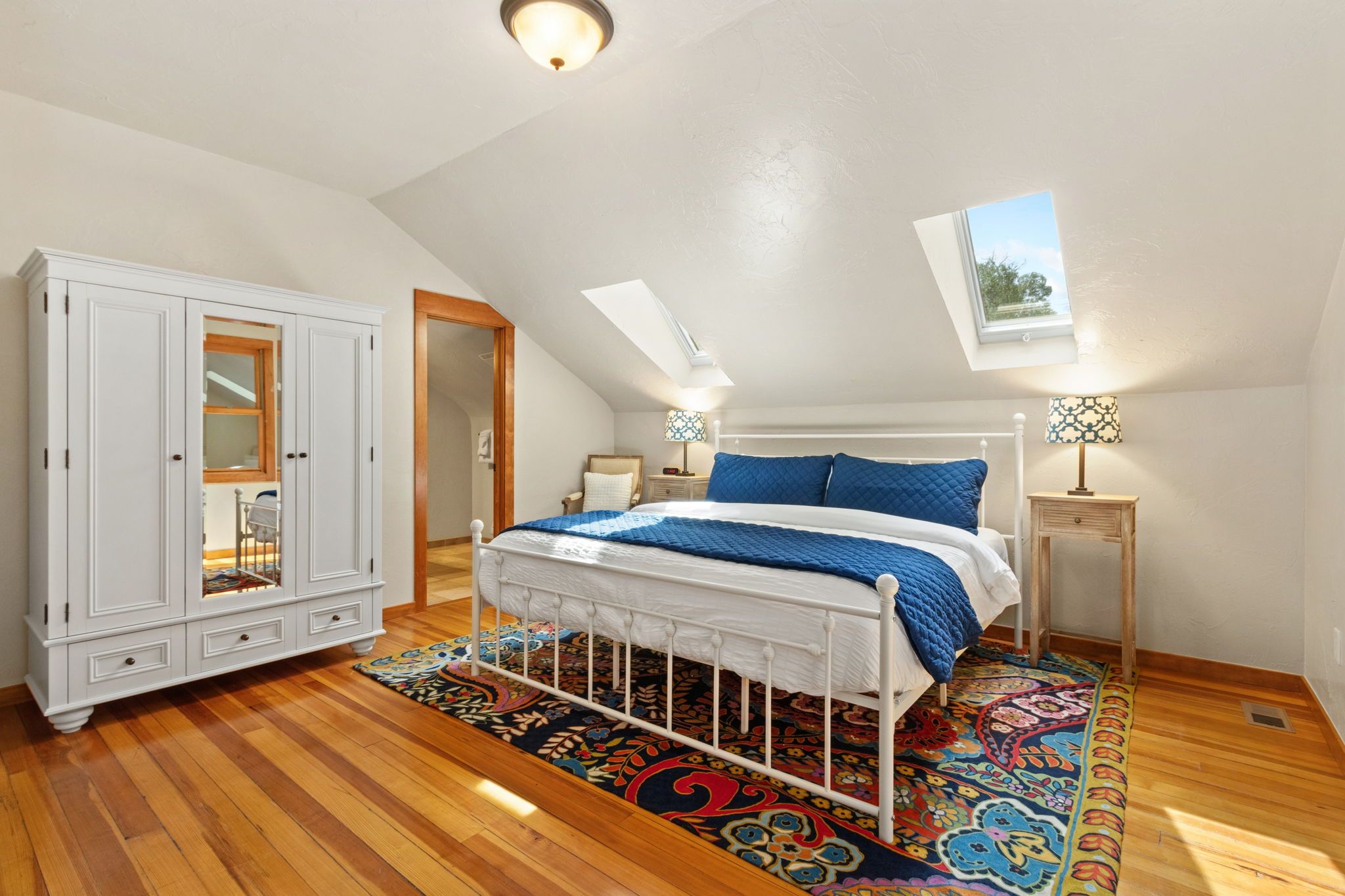 A bedroom with a bed, a wardrobe, a nightstand, a lamp, and a skylight.