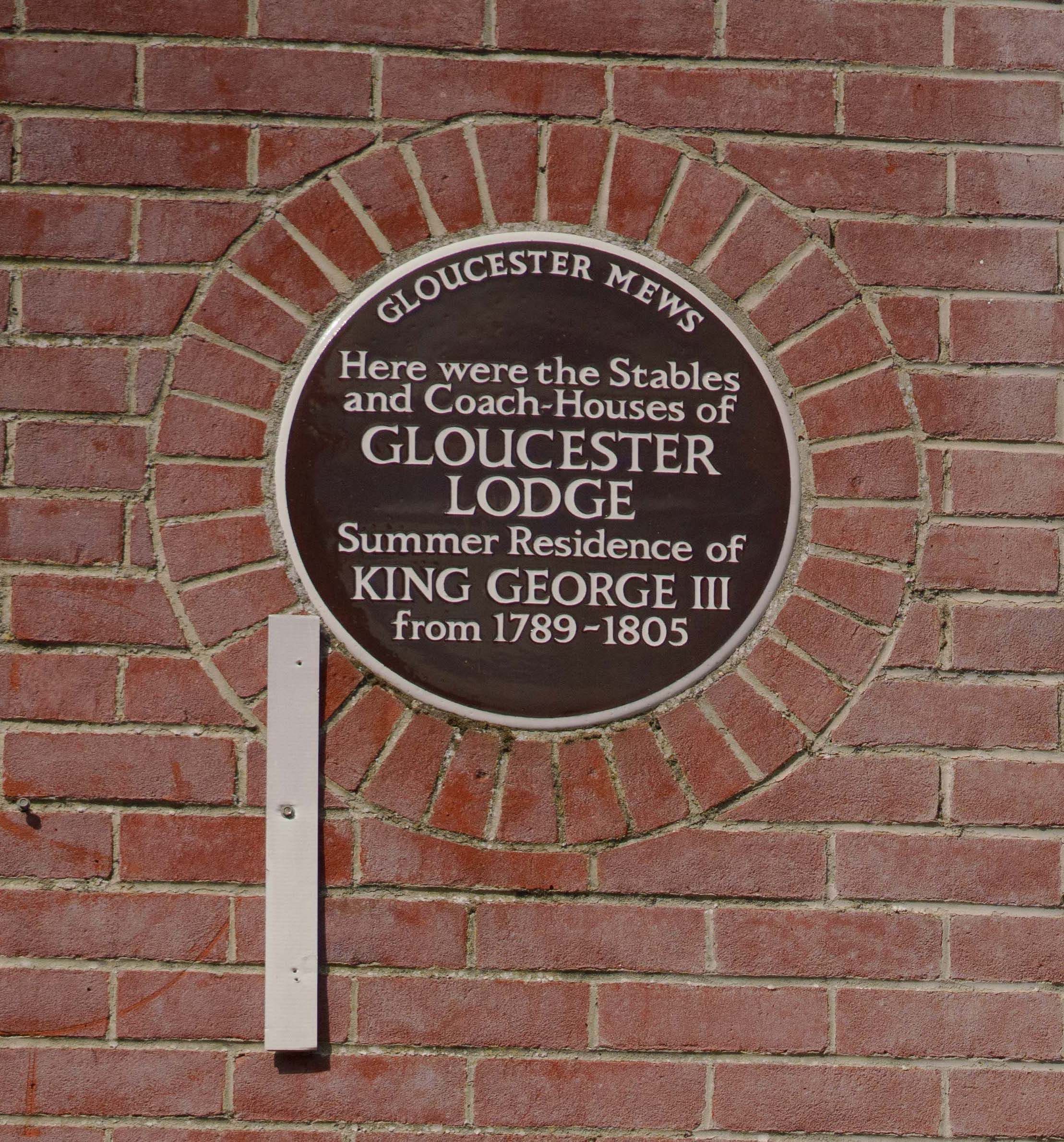 Una placa circular montada en una pared de ladrillo, que detalla Gloucester Lodge como residencia veraniega del rey Jorge III de 1789 a 1805.