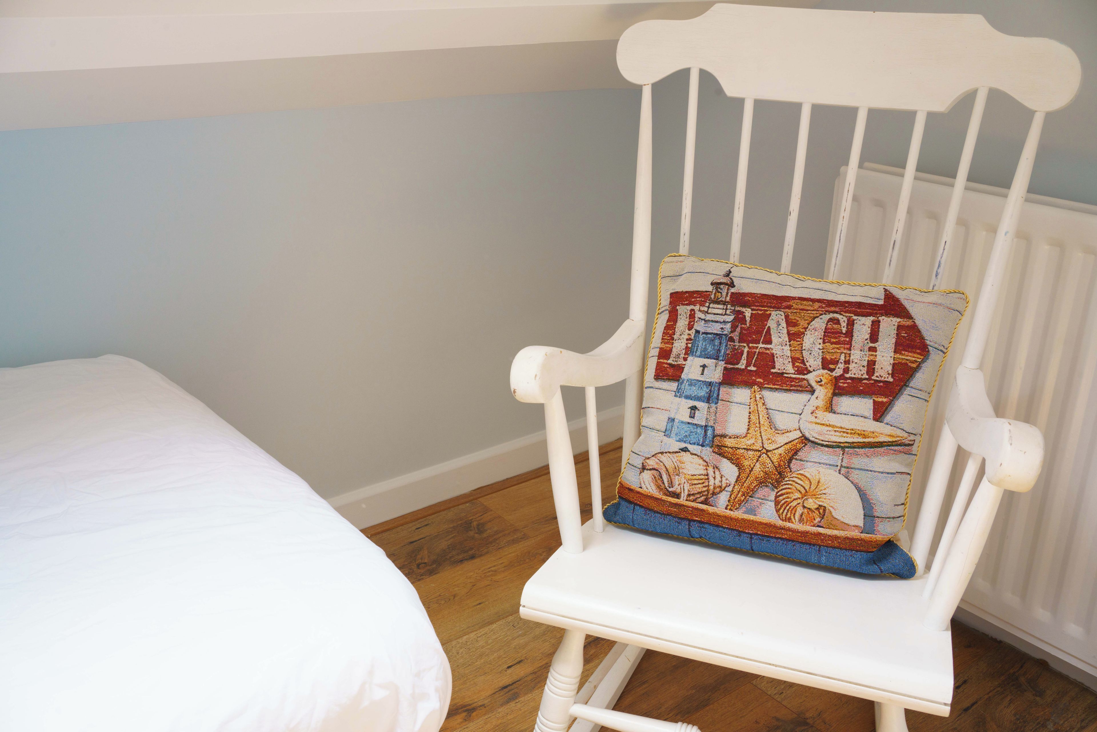 A white rocking chair with a colorful cushion featuring maritime elements.