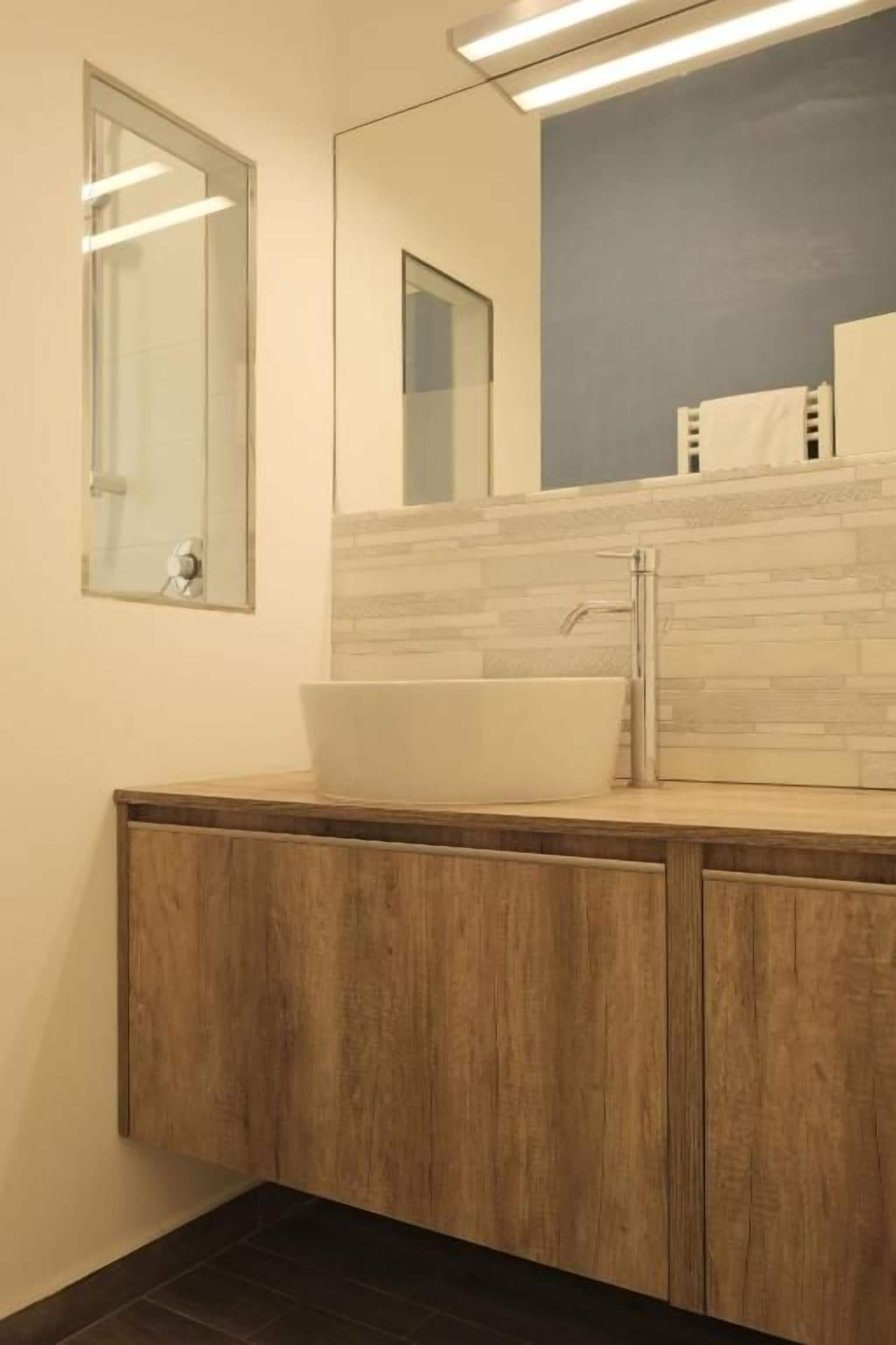 Un baño con tocador de madera, un lavabo blanco y un espejo.