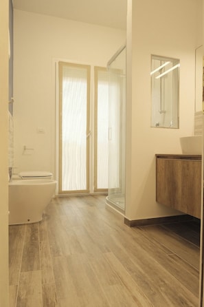 Un baño con inodoro, lavamanos, espejo y zona de ducha.