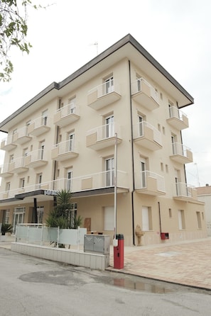 Un edificio de varios pisos con balcones, una entrada cubierta y una zona de estacionamiento.