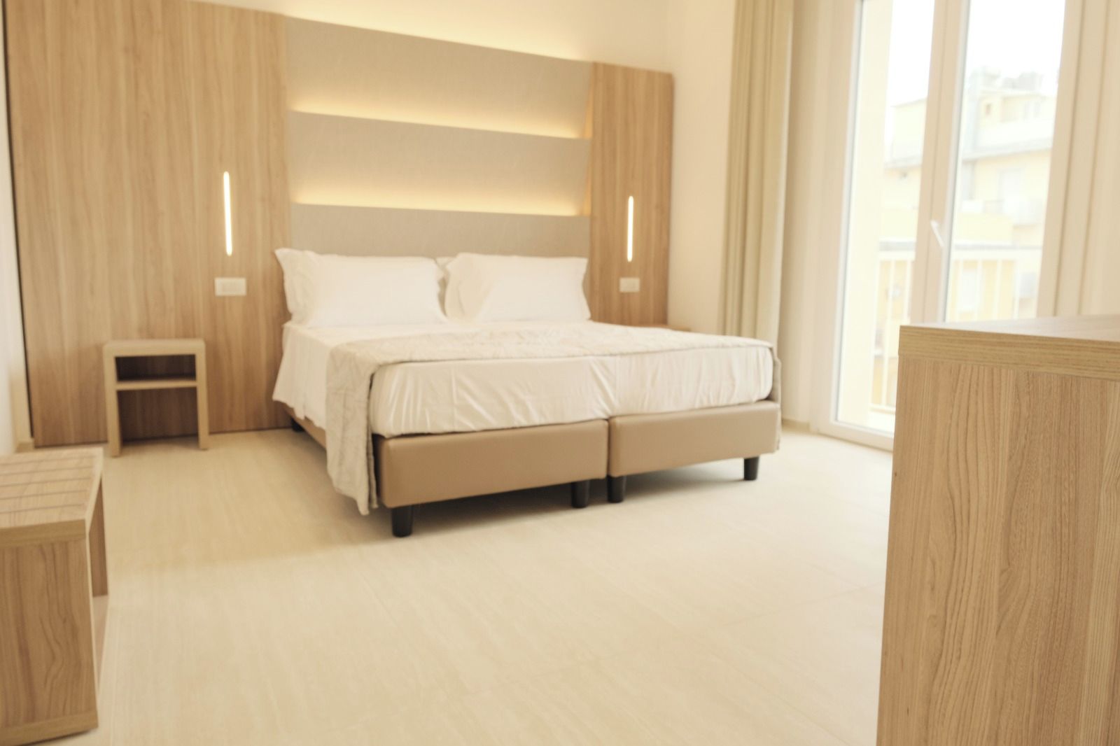 A modern bedroom with a large bed, a nightstand, and a built-in headboard with integrated lighting.