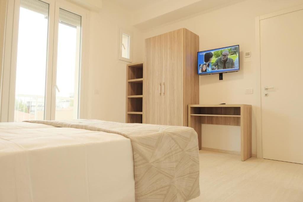 Un dormitorio con cama, televisor montado en la pared y un armario de madera.
