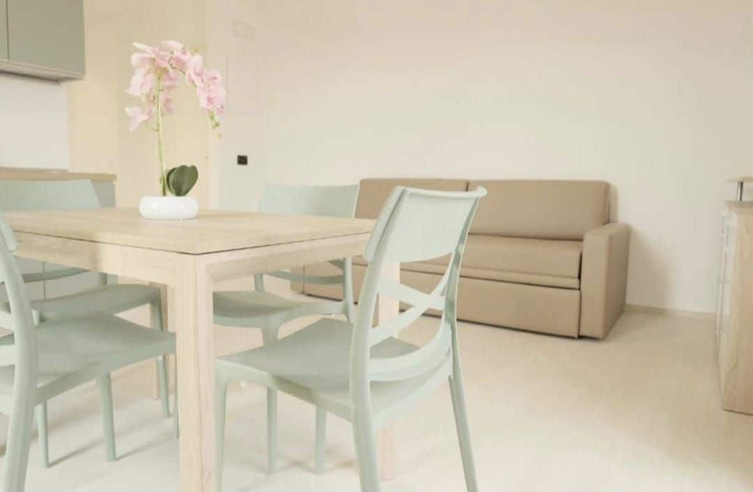 Un comedor con una mesa, sillas, un florero con flores y un sofá.