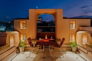 An outdoor dining area with a table and chairs, a potted plant, and a decorative archway. - Indulge Udaipur (Phool Haveli) by PACK (Udaipur)