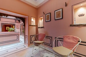 A room with a pink wall, a mirror, and two chairs with patterned cushions. - Indulge Udaipur (Phool Haveli) by PACK (Udaipur)