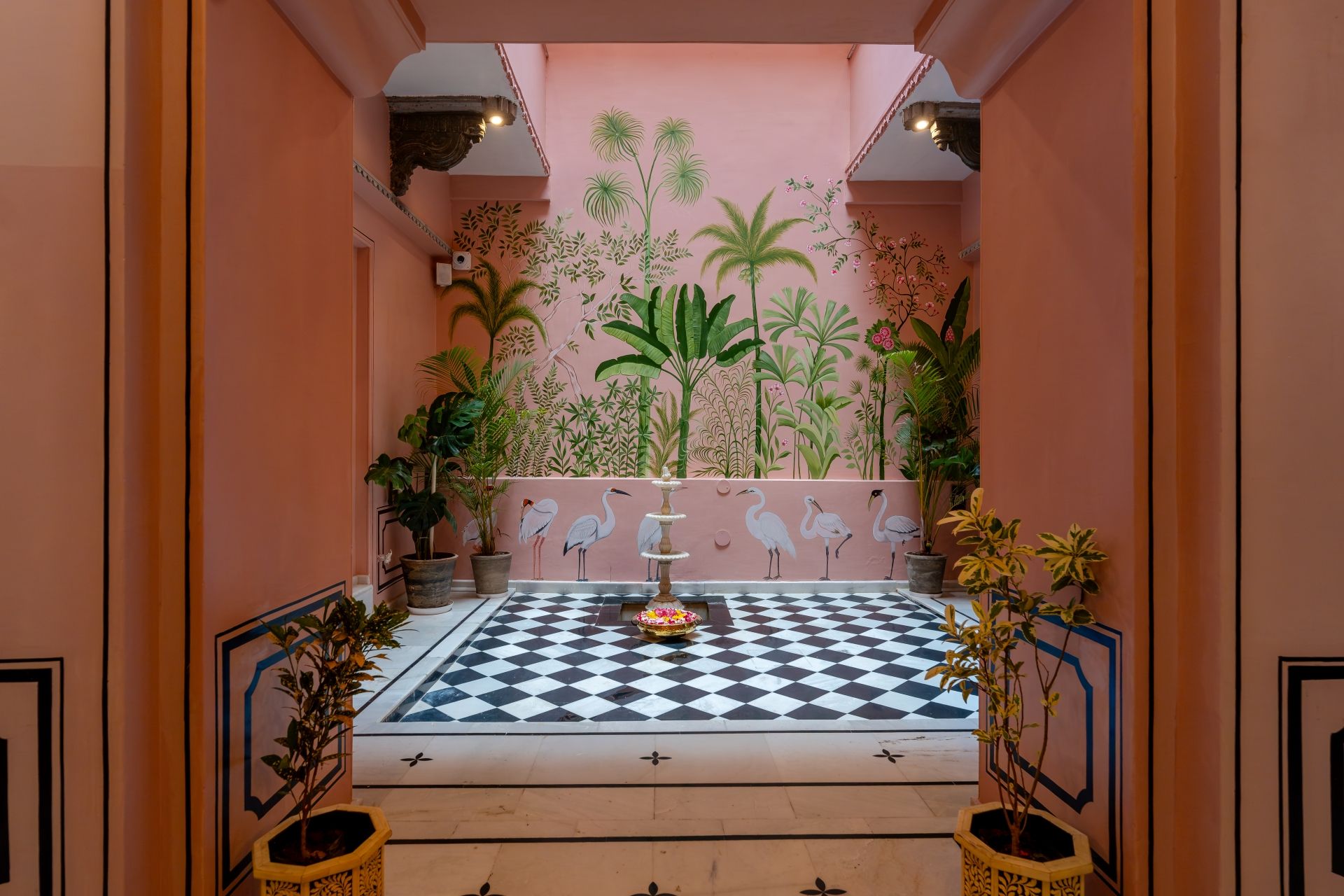 Een kamer met een zwart-witte vloer, een fontein en een muur met afbeeldingen van tropische planten.