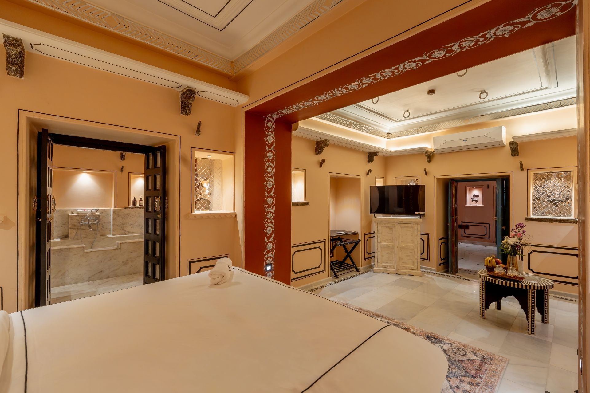 Habitación de hotel con cama, televisor, escritorio y silla, y baño con espejo y lavamanos.