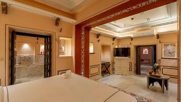 Habitación de hotel con cama, televisor, escritorio y silla, y baño con espejo y lavamanos.