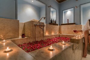 Ein Spa-Raum mit einer Marmorbadewanne, Kerzen und Rosenblüten.