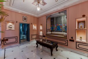 A hotel lobby with a marble floor, a sofa with cushions, a coffee table, and decorative wall sconces. - Indulge Udaipur (Phool Haveli) by PACK (Udaipur)